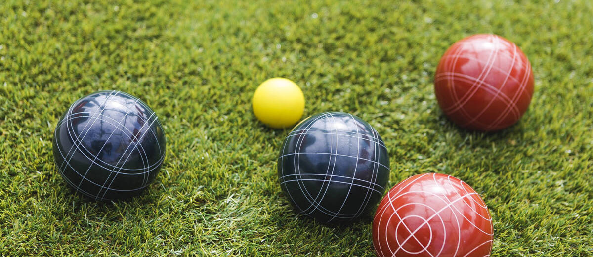 Red, yellow and black bocce balls rest on the grass.