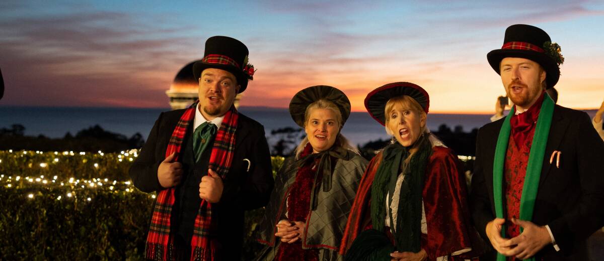 Four standing and singing Christmas Carolers during sunset